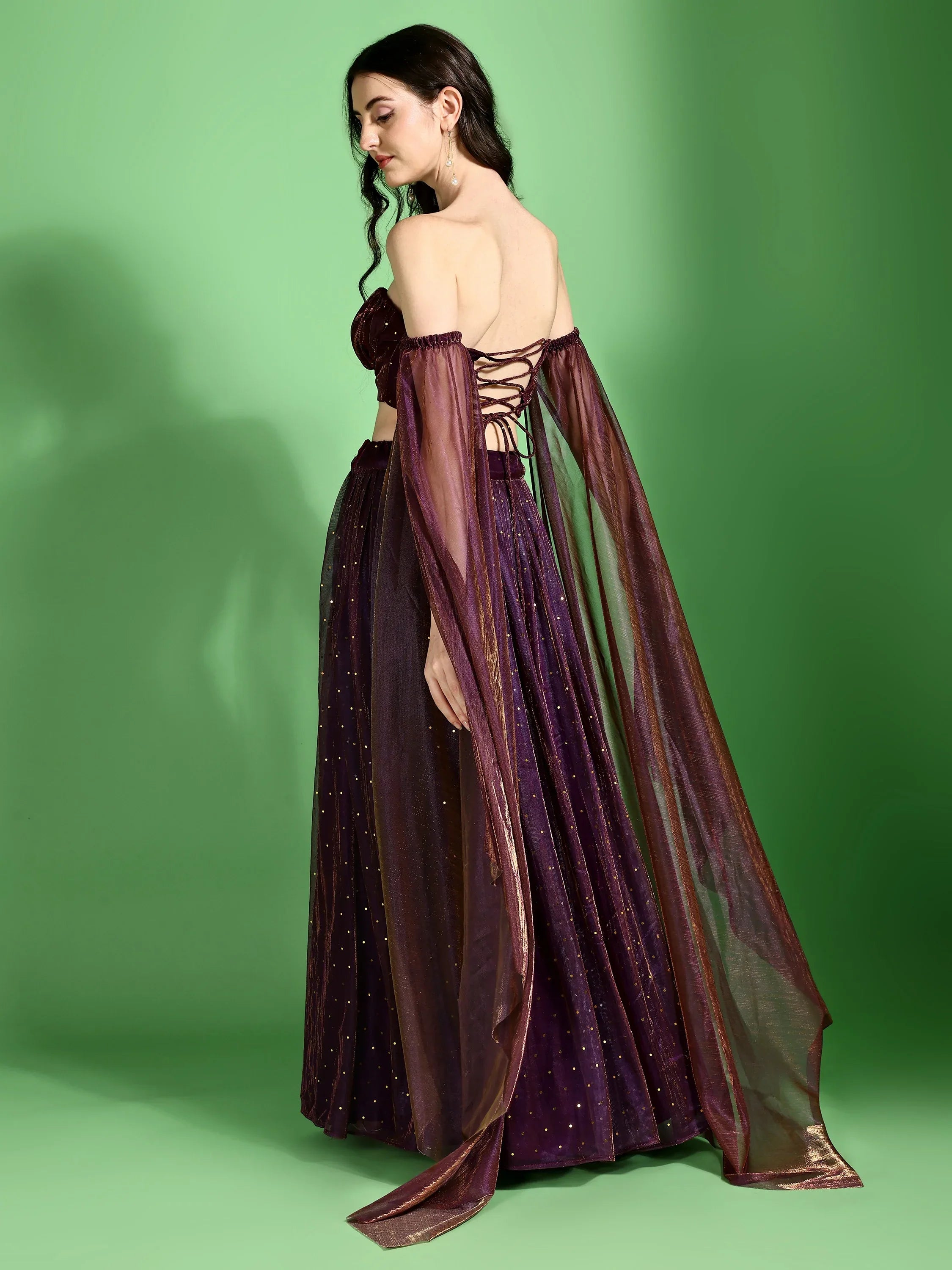 Woman wearing a dark purple outfit with sheer sleeves against a green background Glanzavi