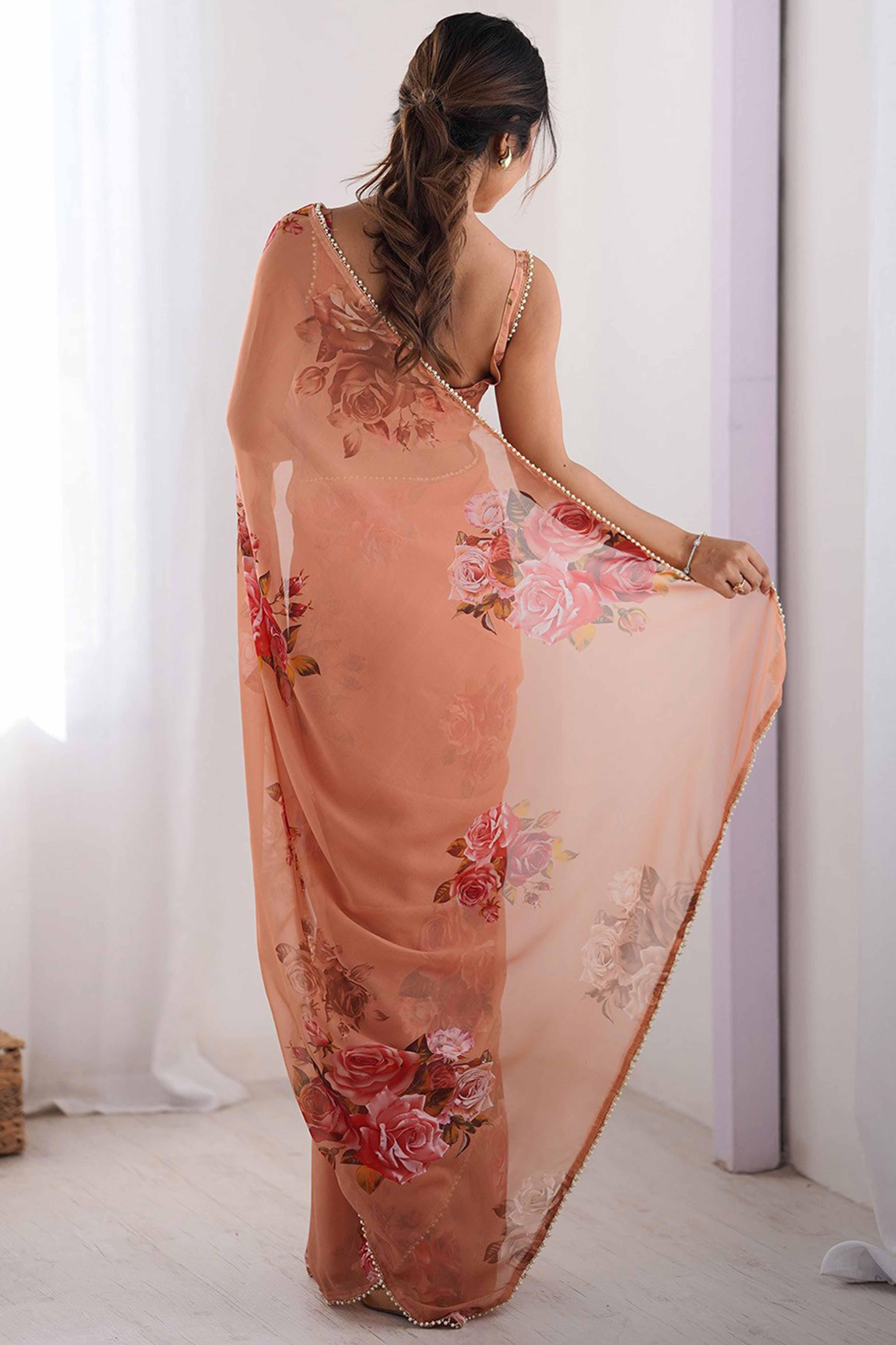 Woman wearing a peach floral saree against a white curtain background Glanzavi
