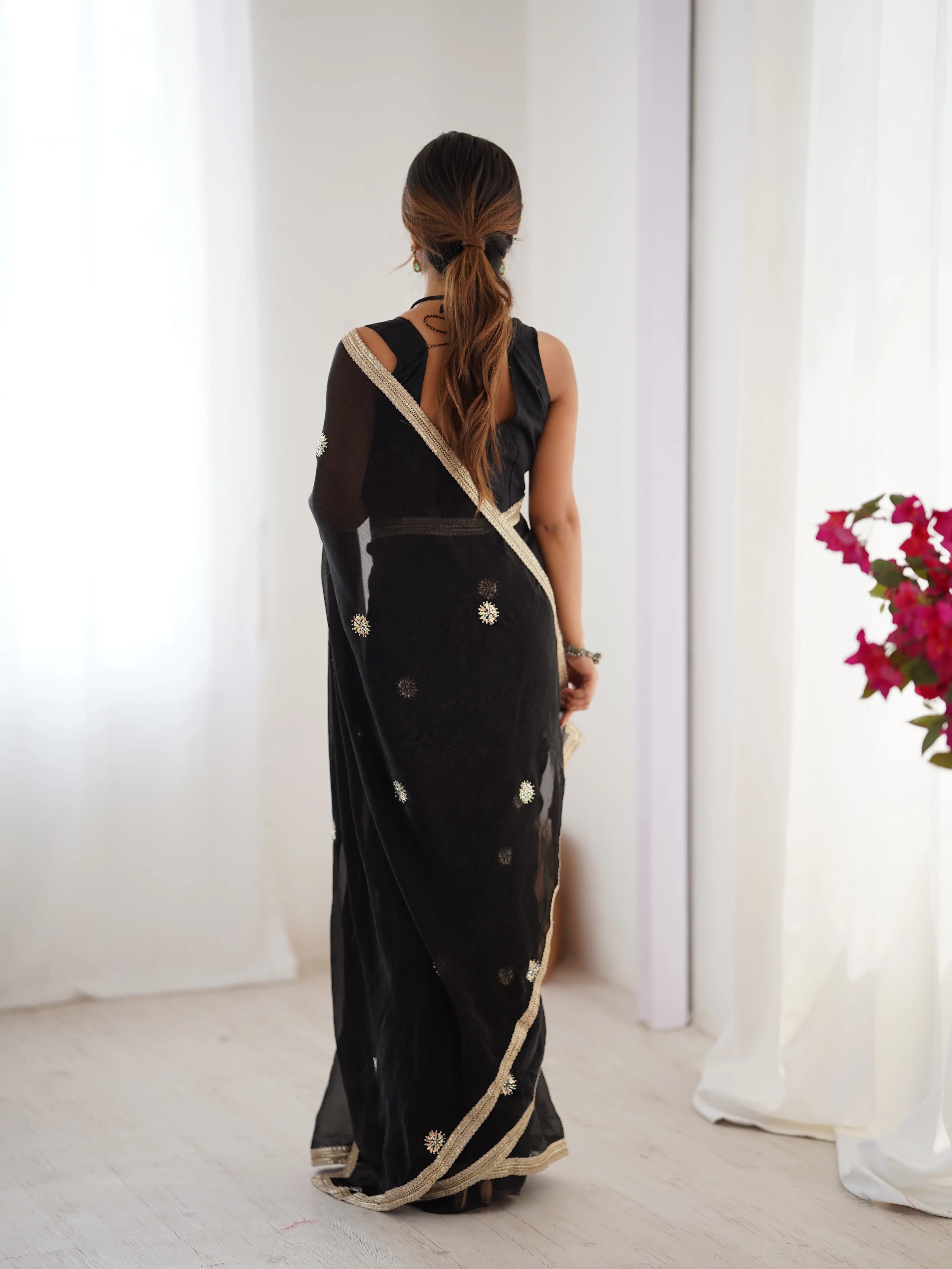 Woman wearing a black saree with gold border in a minimal indoor setting Glanzavi