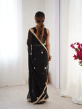 Woman wearing a black saree with gold border in a minimal indoor setting Glanzavi