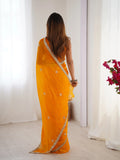 Woman wearing a bright yellow saree with a white border in a minimal indoor setting Glanzavi.
