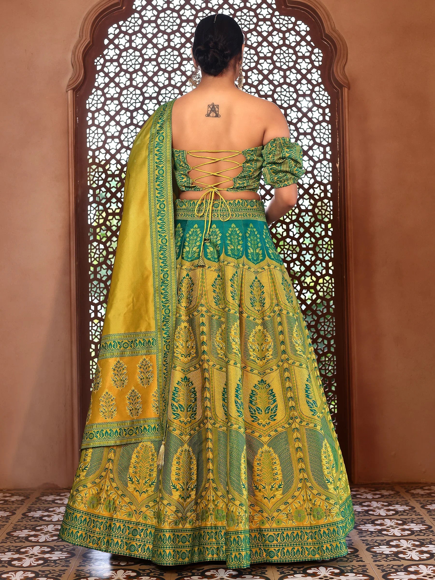 Woman wearing a green and yellow embroidered traditional outfit in front of an ornate window Glanzavi.