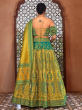 Woman wearing a green and yellow embroidered traditional outfit in front of an ornate window Glanzavi.