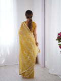 Woman wearing a yellow saree with white floral patterns against a white background Glanzavi