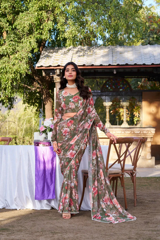 Woman in a floral saree standing outdoors with greenery and a building in the background Glanzavi