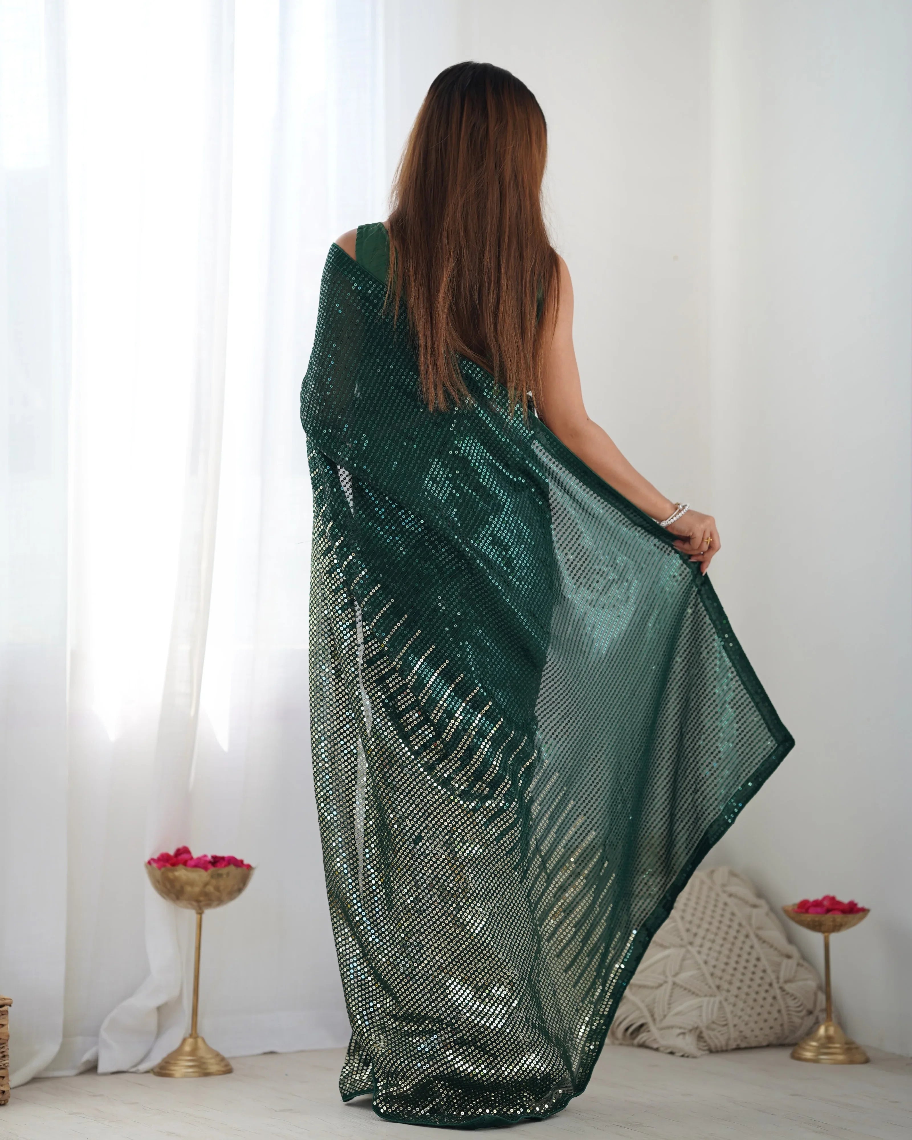 Woman holding a green saree in a minimalistic room with white curtains and decorative items Glanzavi