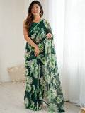 Woman wearing a green floral dress holding a matching scarf indoors Glanzavi.