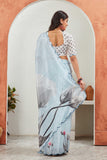 Woman wearing a light blue saree with floral patterns in a room with an archway Glanzavi