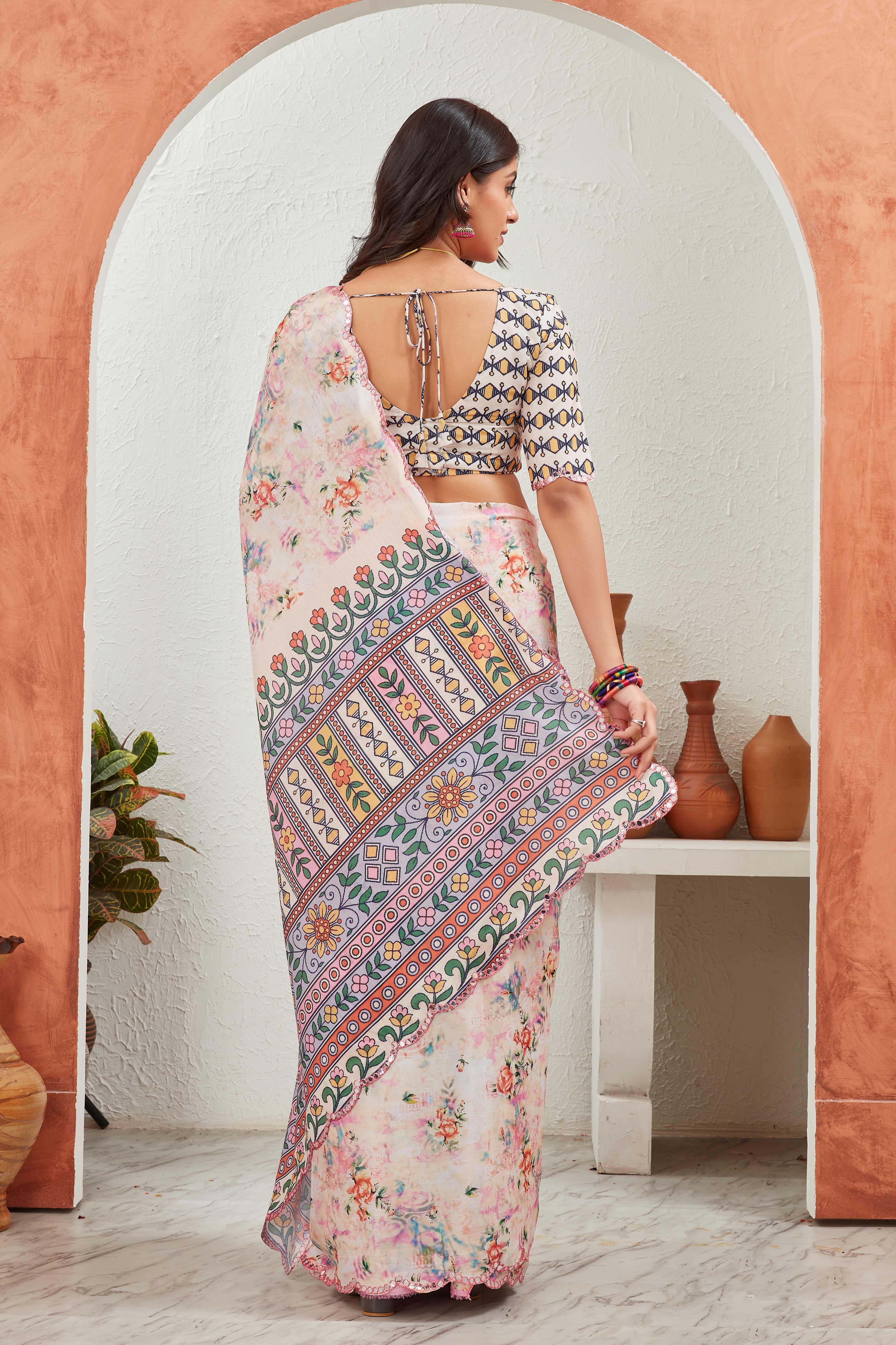 Woman in a traditional saree with a colorful pattern, standing in a room with a white wall and wooden shelf Glanzavi