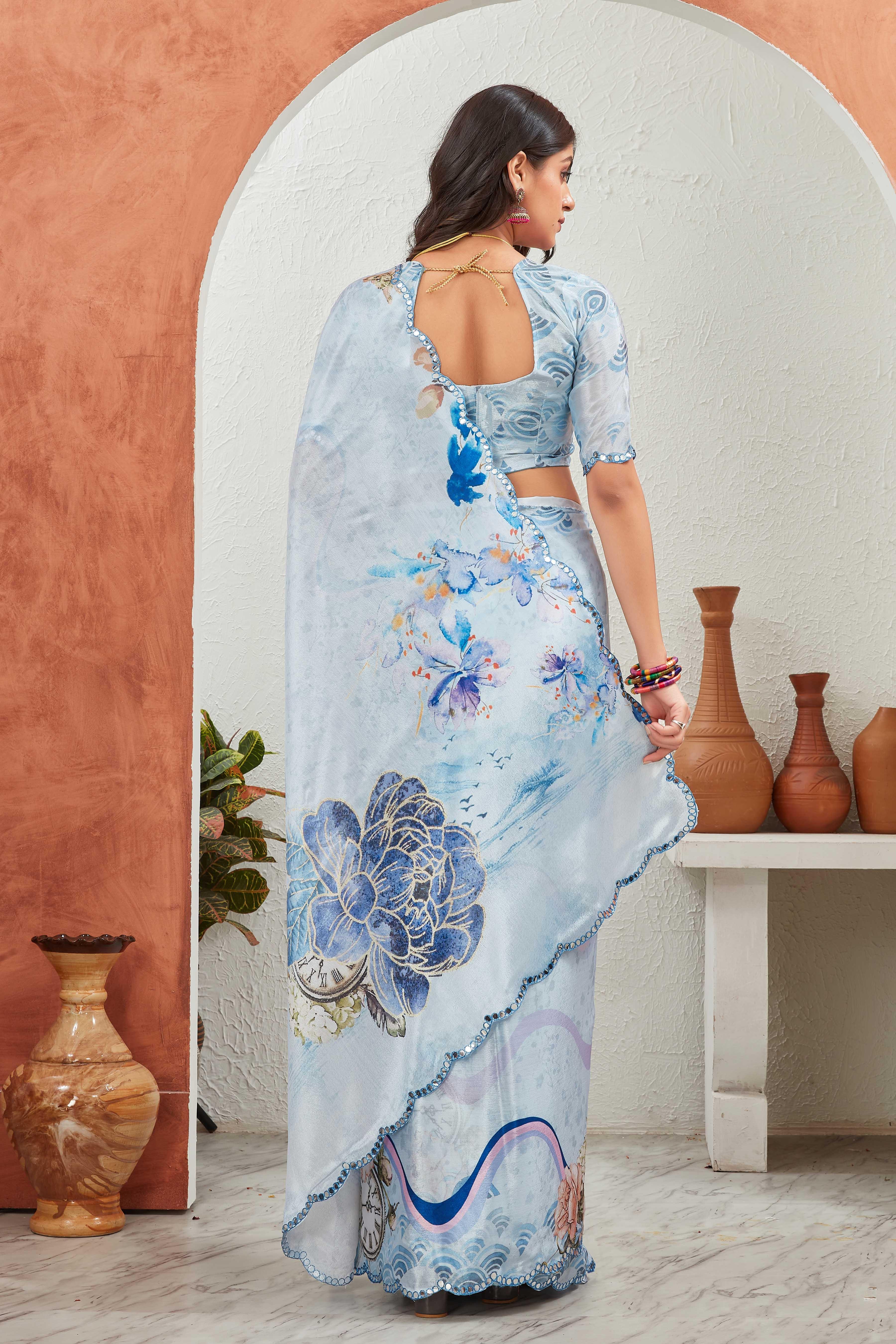 Woman wearing a light blue saree with floral patterns in a room with decorative vases Glanzavi