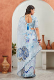 Woman wearing a light blue saree with floral patterns in a room with decorative vases Glanzavi