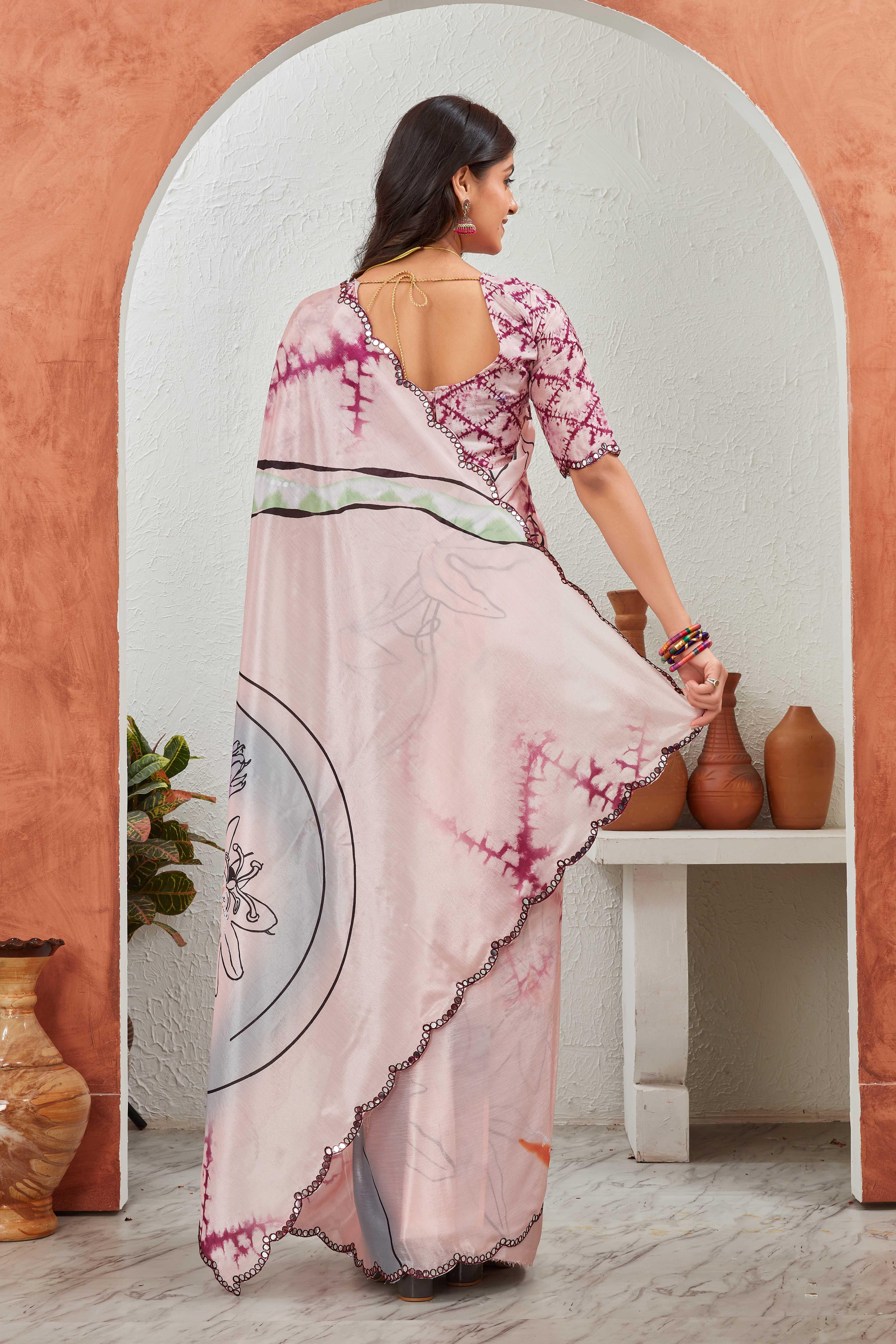 Woman in a pink and white saree with a floral pattern, standing in a room with a white archway and orange walls Glanzavi