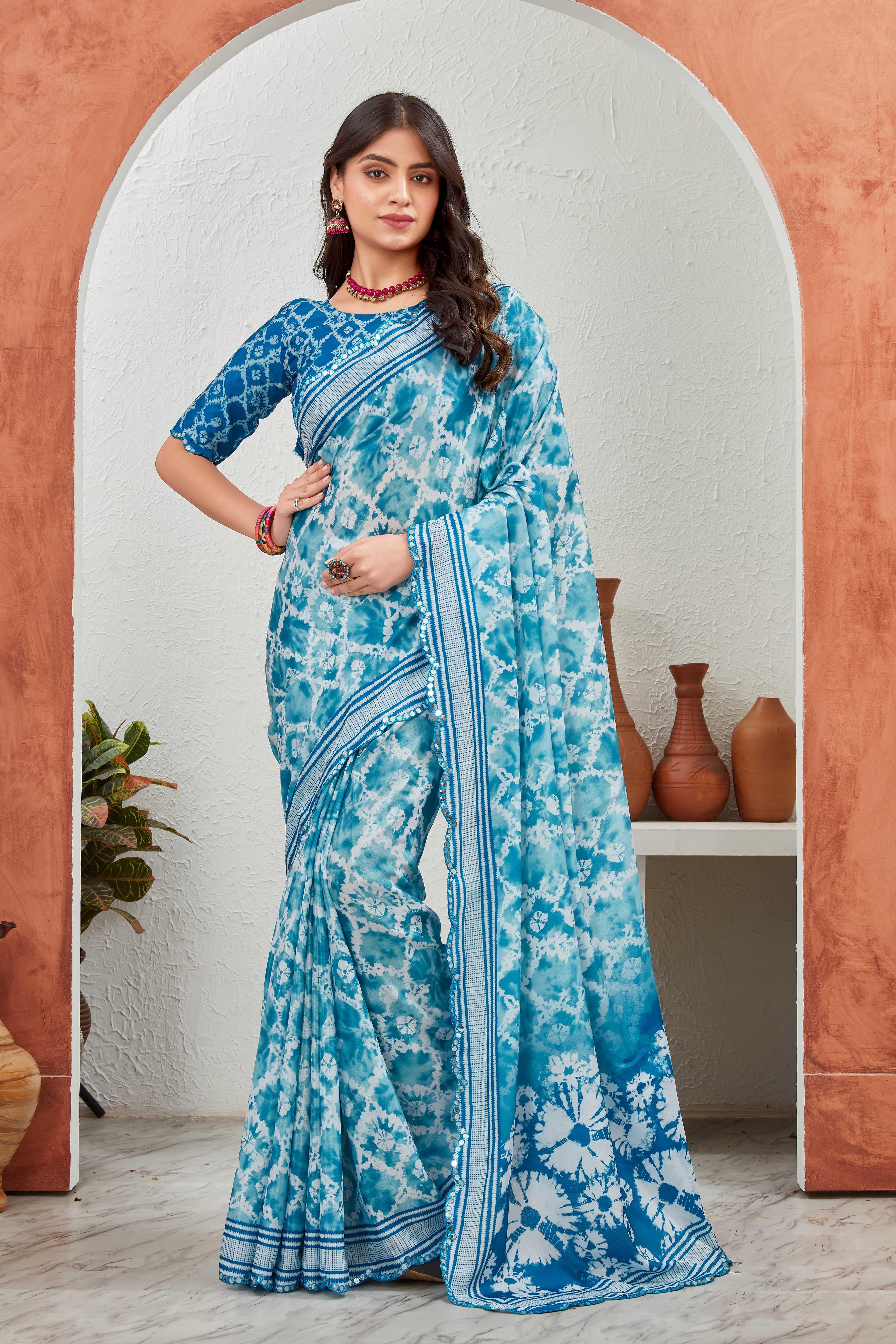 Woman wearing a blue and white saree standing in front of a decorative archway Glanzavi