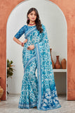 Woman wearing a blue and white saree standing in front of a decorative archway Glanzavi