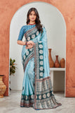 Woman wearing a blue saree with a patterned border in a room with decorative vases Glanzavi