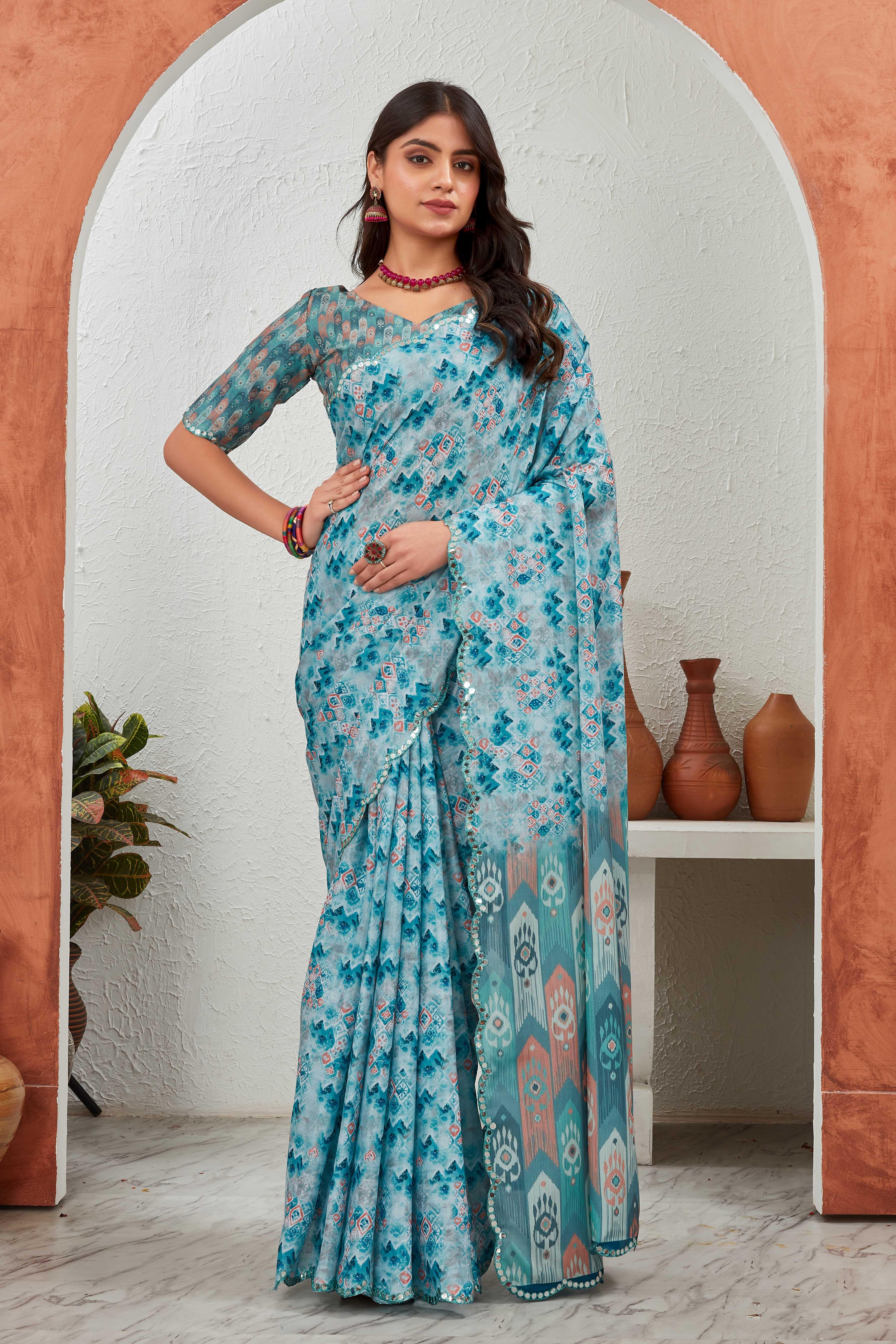 Woman wearing a blue floral saree standing in front of an archway with decorative pots Glanzavi