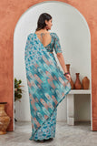 Woman in a floral saree standing in front of a mirror with decorative vases on a shelf Glanzavi