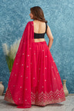 Woman wearing a red lehenga with a black blouse against a blue textured wall Glanzavi