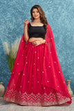 Woman wearing a red embroidered lehenga with a black blouse against a blue textured background Glanzavi