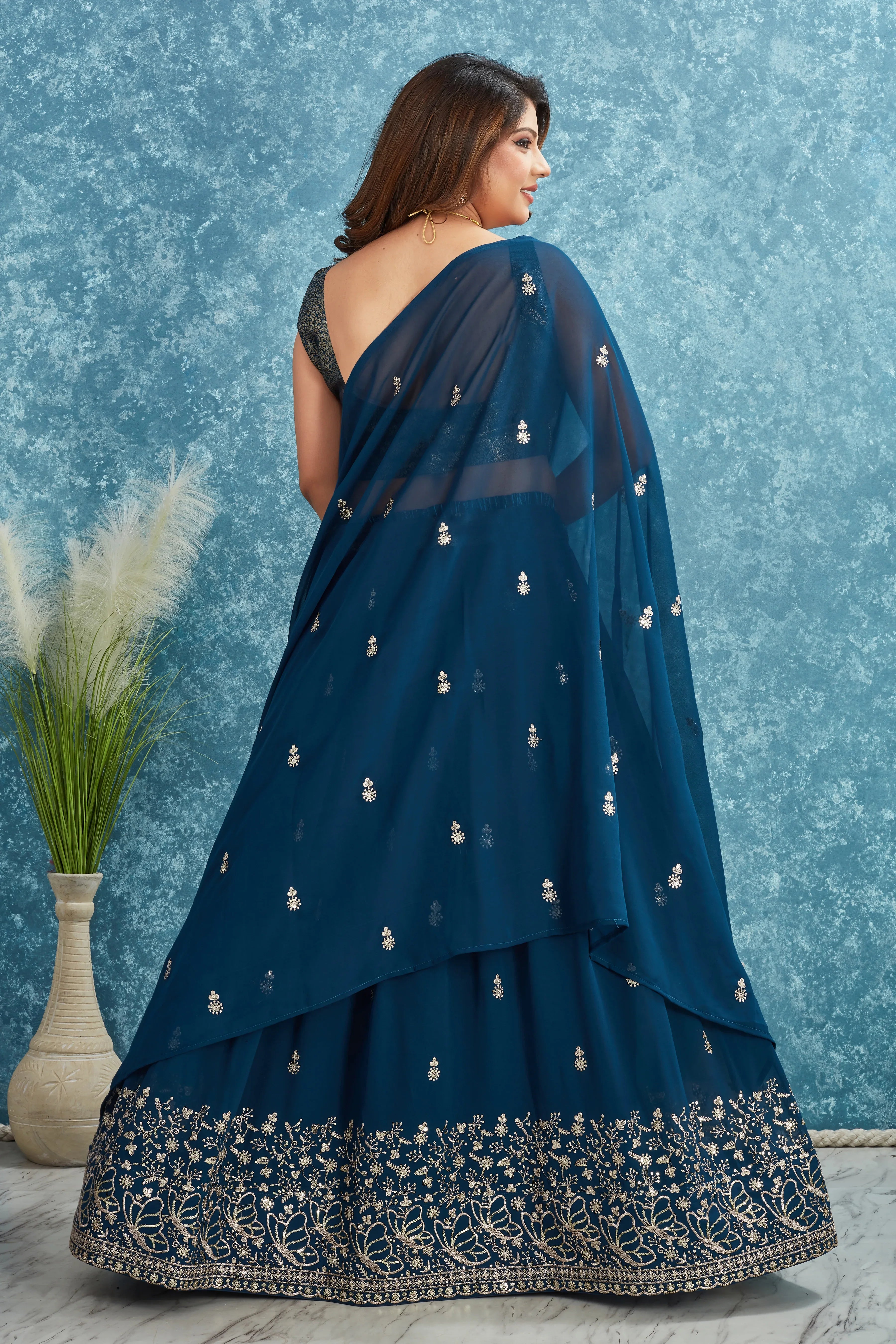 Woman wearing a dark blue saree with silver embroidery against a textured blue wall Glanzavi.