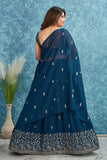 Woman wearing a dark blue saree with silver embroidery against a textured blue wall Glanzavi.