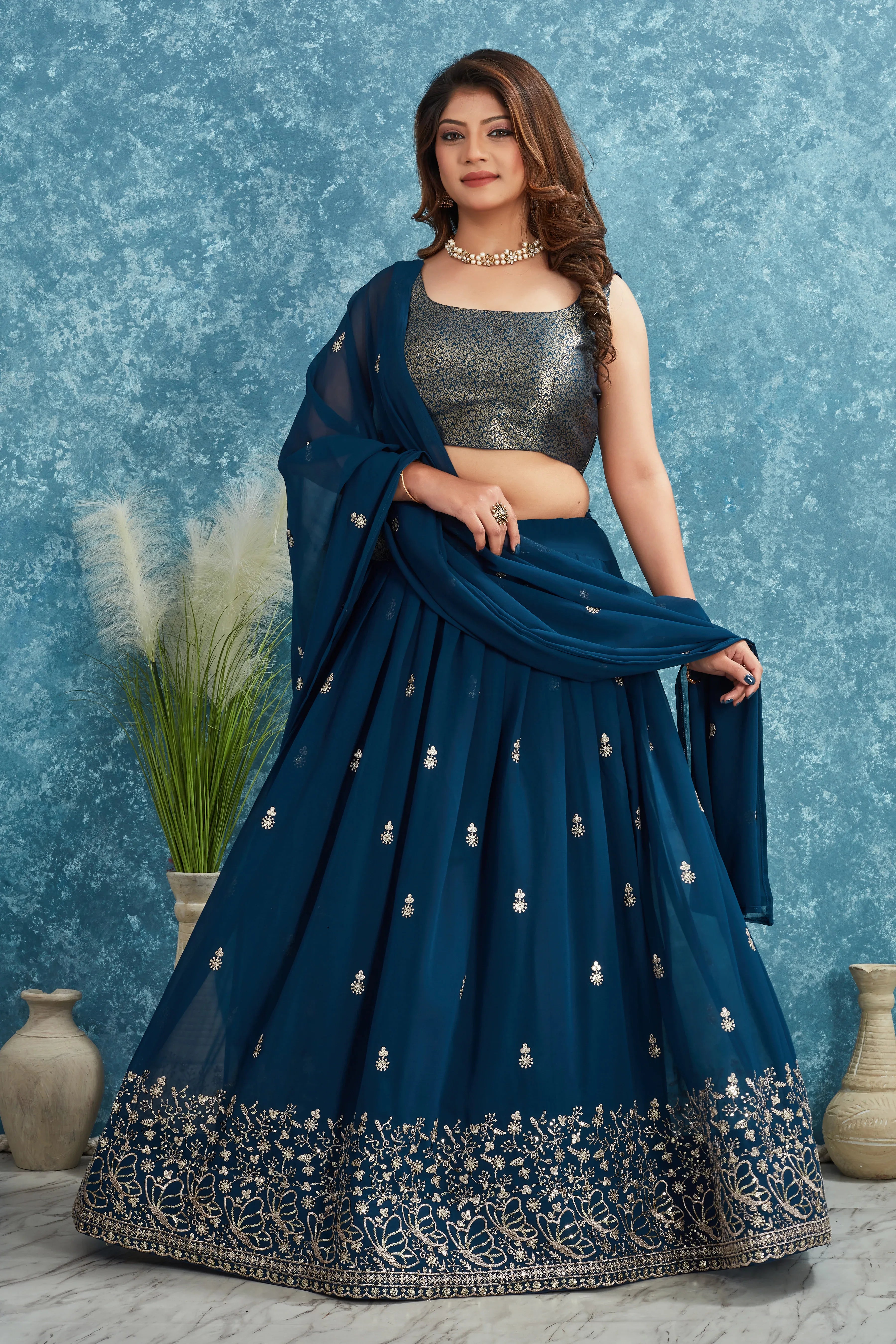 Woman wearing a blue embroidered saree with a silver blouse against a textured blue background Glanzavi