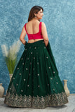 Woman wearing a green lehenga with a red blouse against a blue textured wall Glanzavi