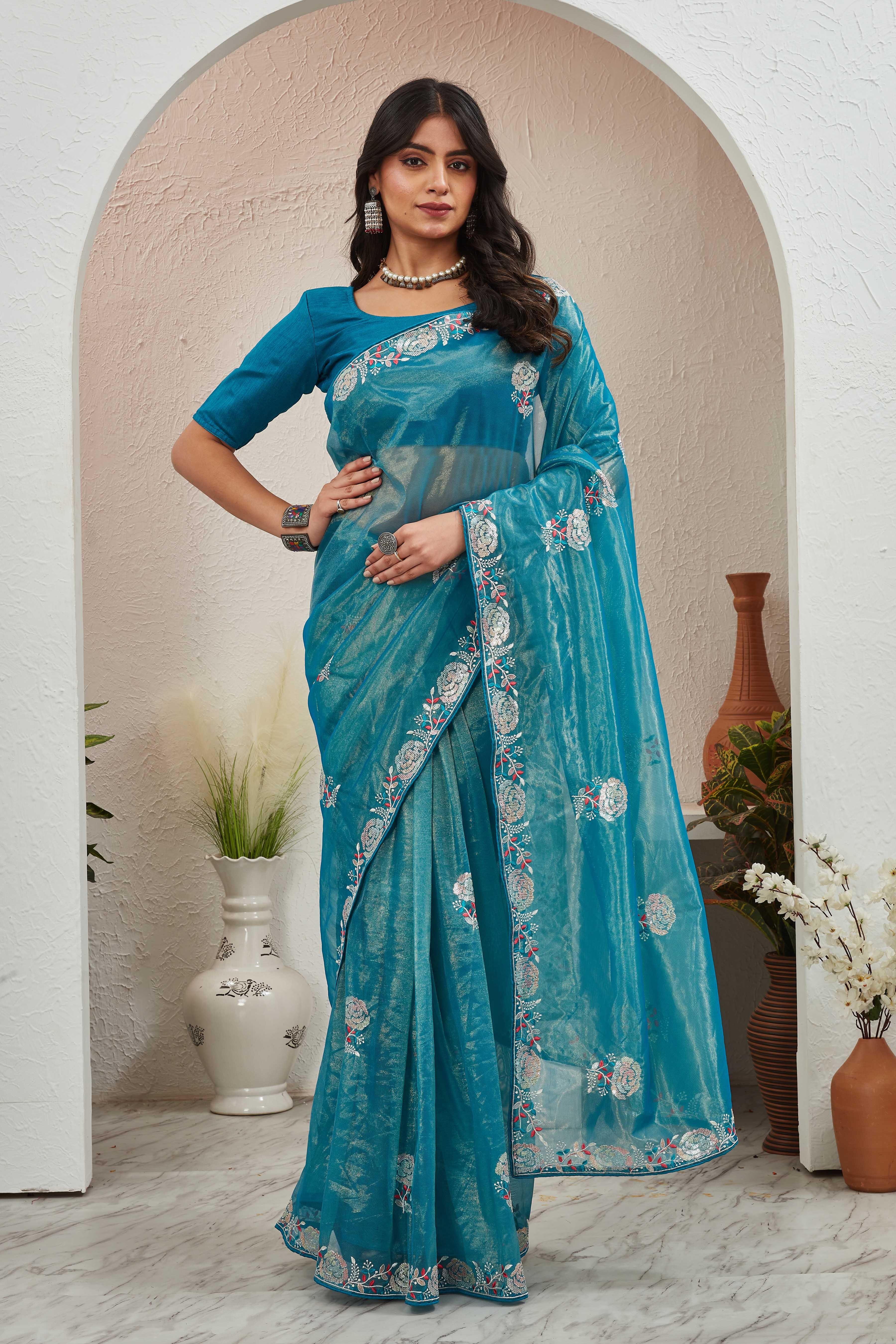 Woman wearing a blue saree with a floral pattern indoors Glanzavi.