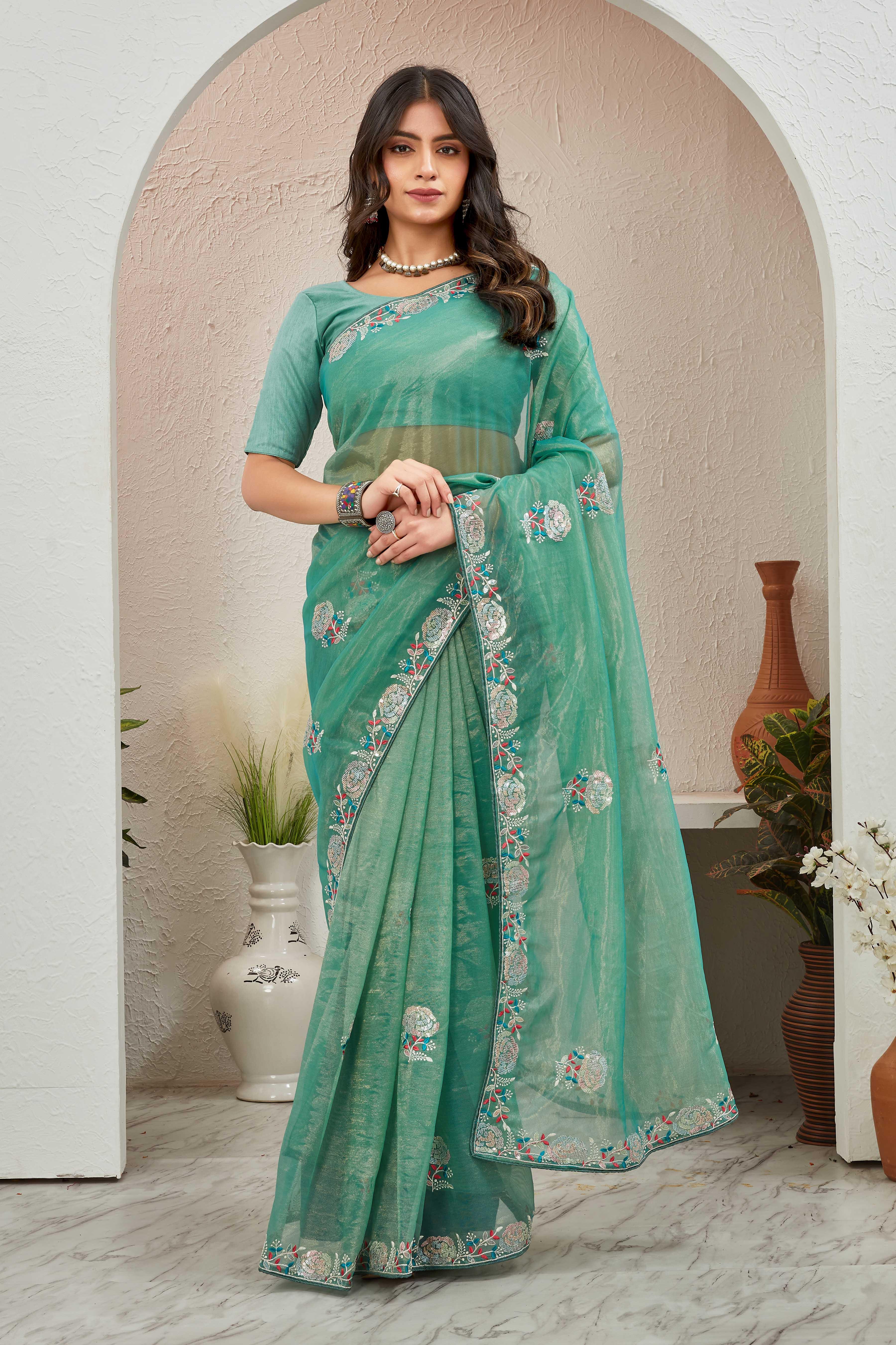 Woman wearing a teal saree with a floral border in an indoor setting Glanzavi.