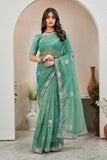 Woman wearing a teal saree with a floral border in an indoor setting Glanzavi.