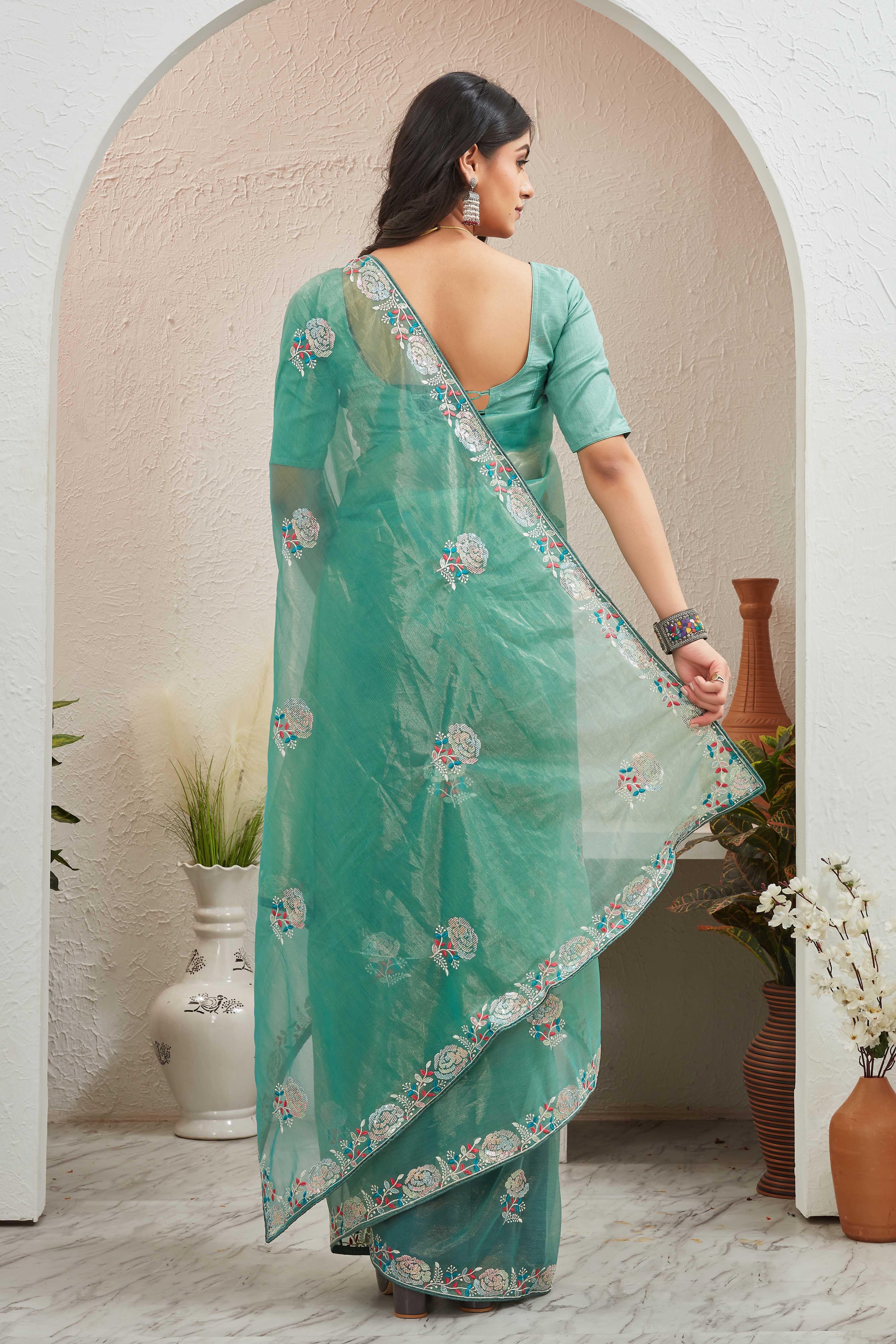 Woman wearing a teal saree with floral patterns in an indoor setting Glanzavi.