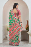 Woman wearing a red and green patterned saree standing in a room with decorative elements Glanzavi
