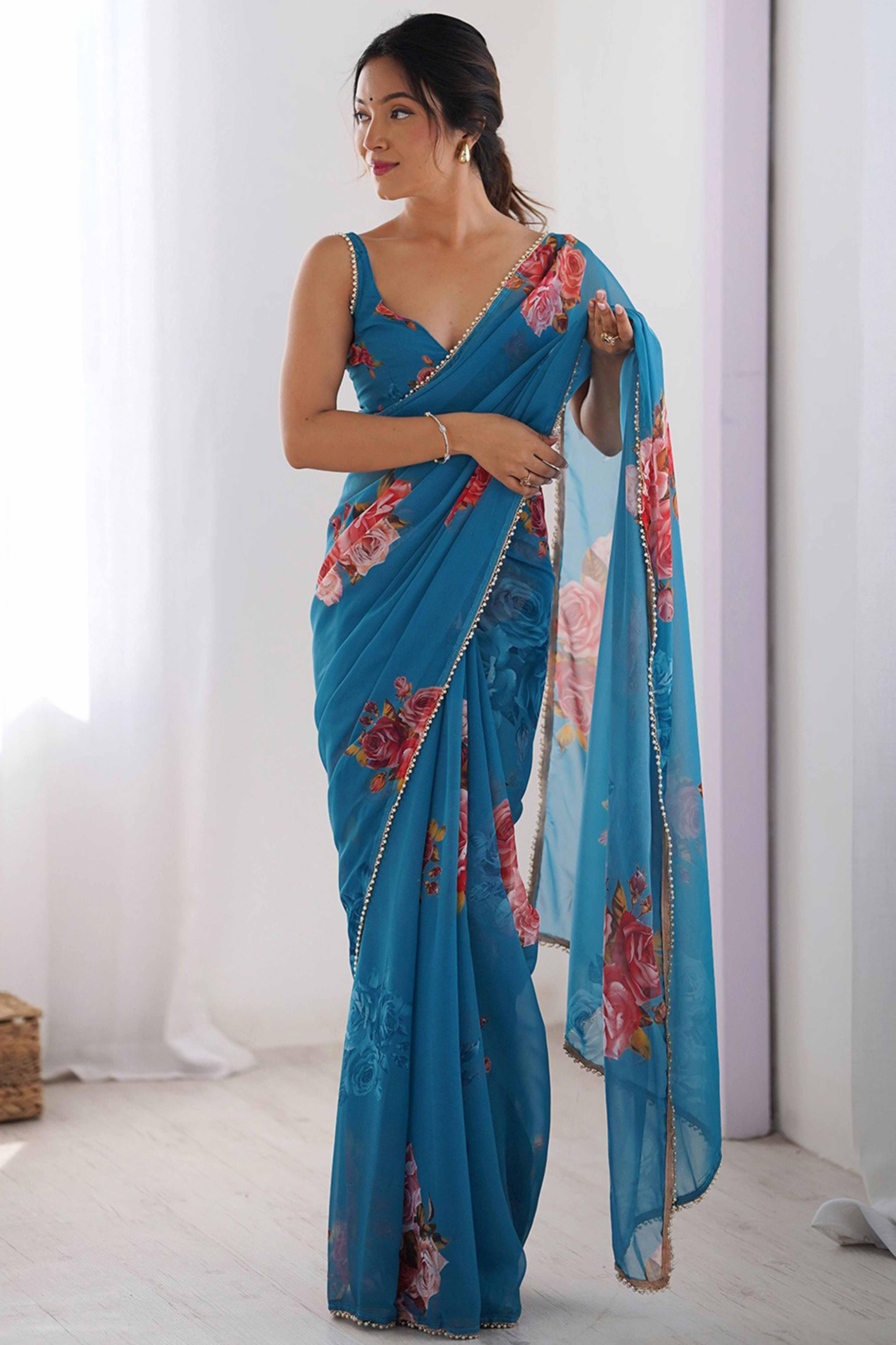 Woman wearing a blue saree with floral patterns in a bright room Glanzavi.