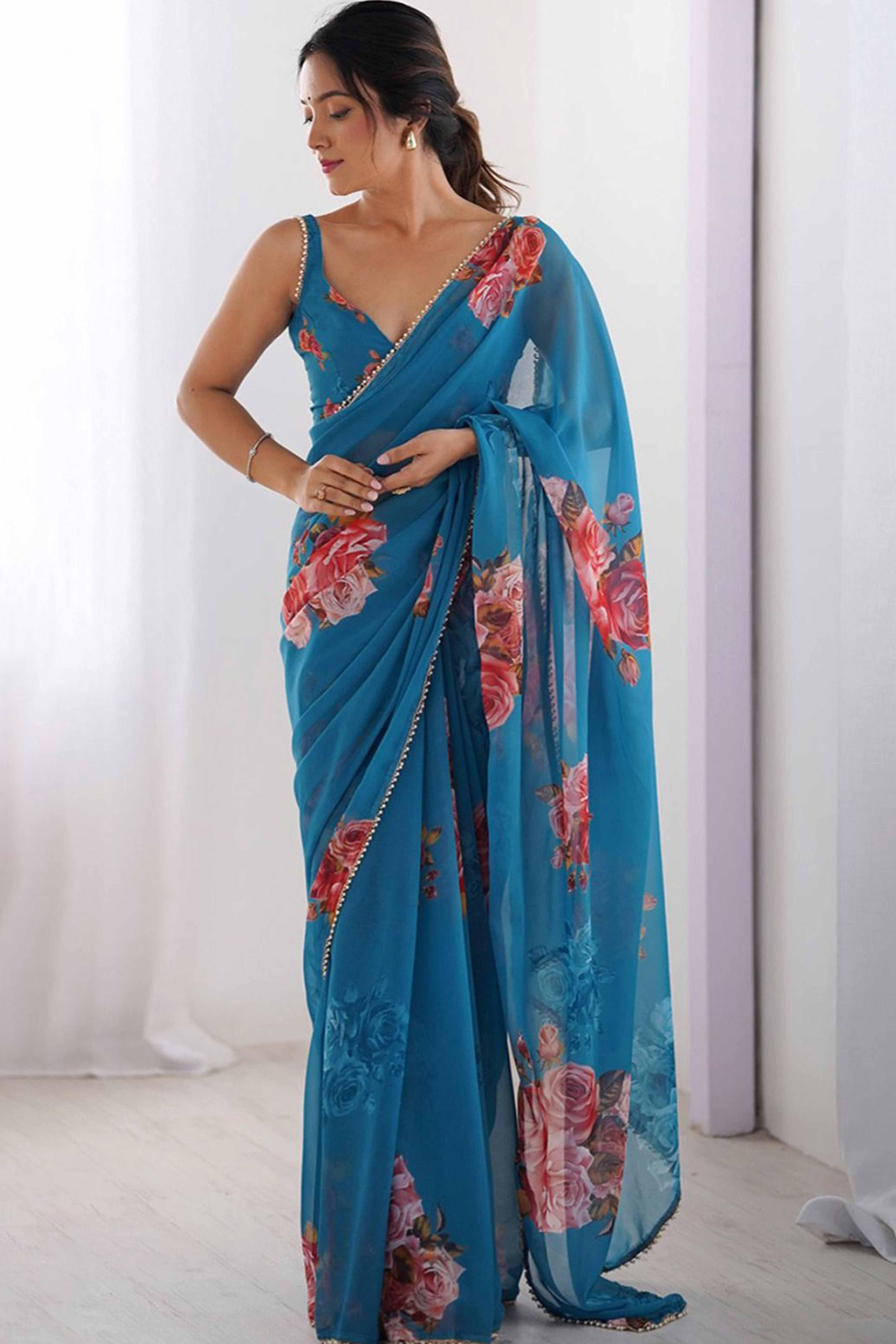 Woman wearing a blue saree with floral patterns against a white background Glanzavi