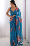 Woman wearing a blue saree with floral patterns against a white background Glanzavi