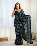 Woman wearing a dark green saree with a geometric pattern in a well-lit room Glanzavi