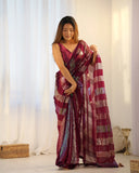 Woman holding a maroon saree with white and gold patterns in a well-lit room Glanzavi
