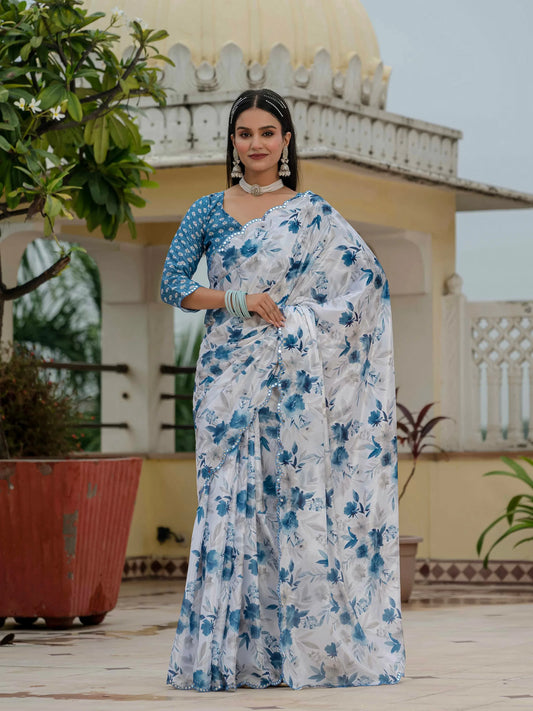 Woman in a blue and white floral saree standing on a rooftop with plants and architectural elements in the background Glanzavi.