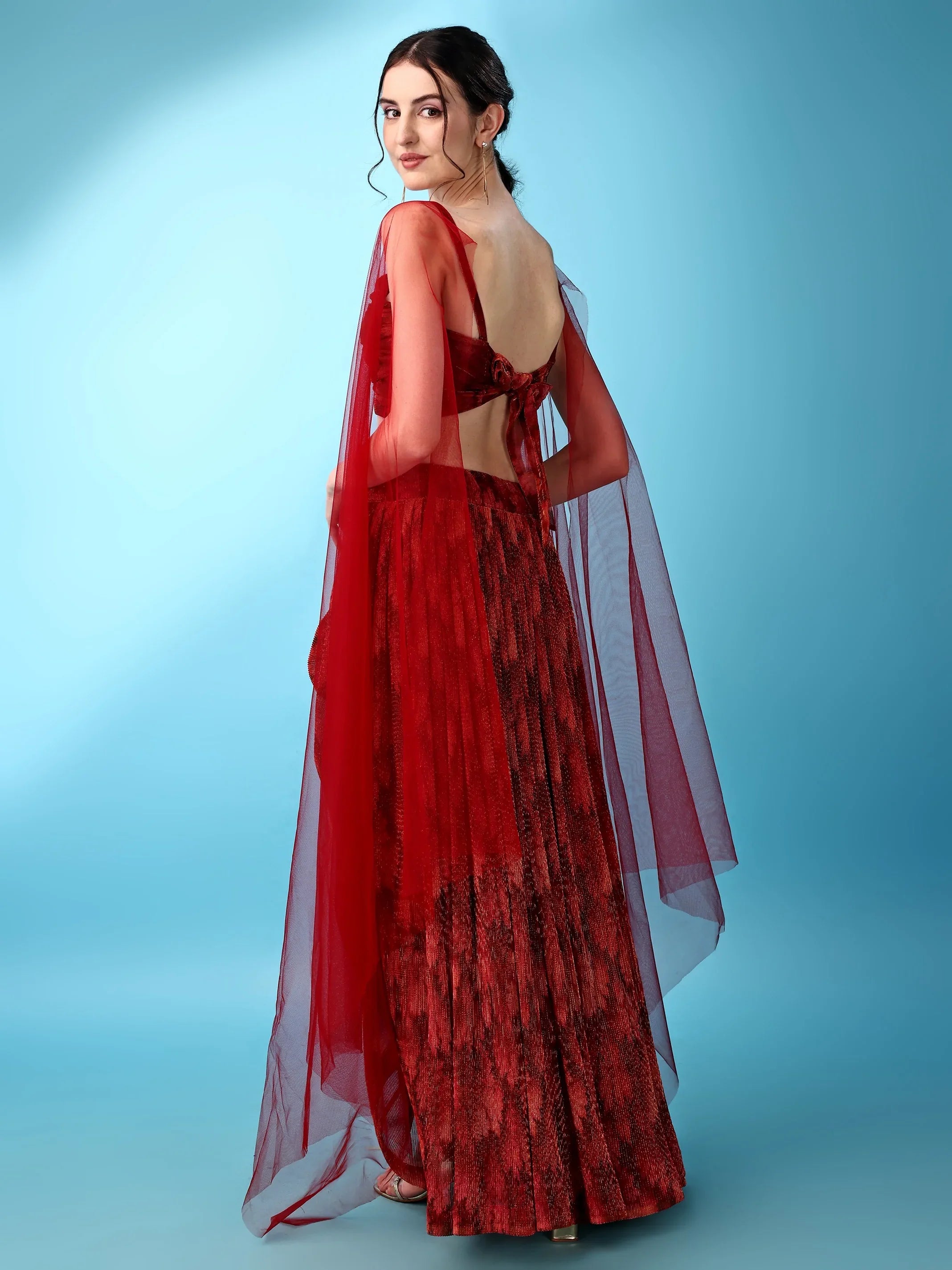 Woman wearing a red evening gown with sheer overlay on a light blue background Glanzavi