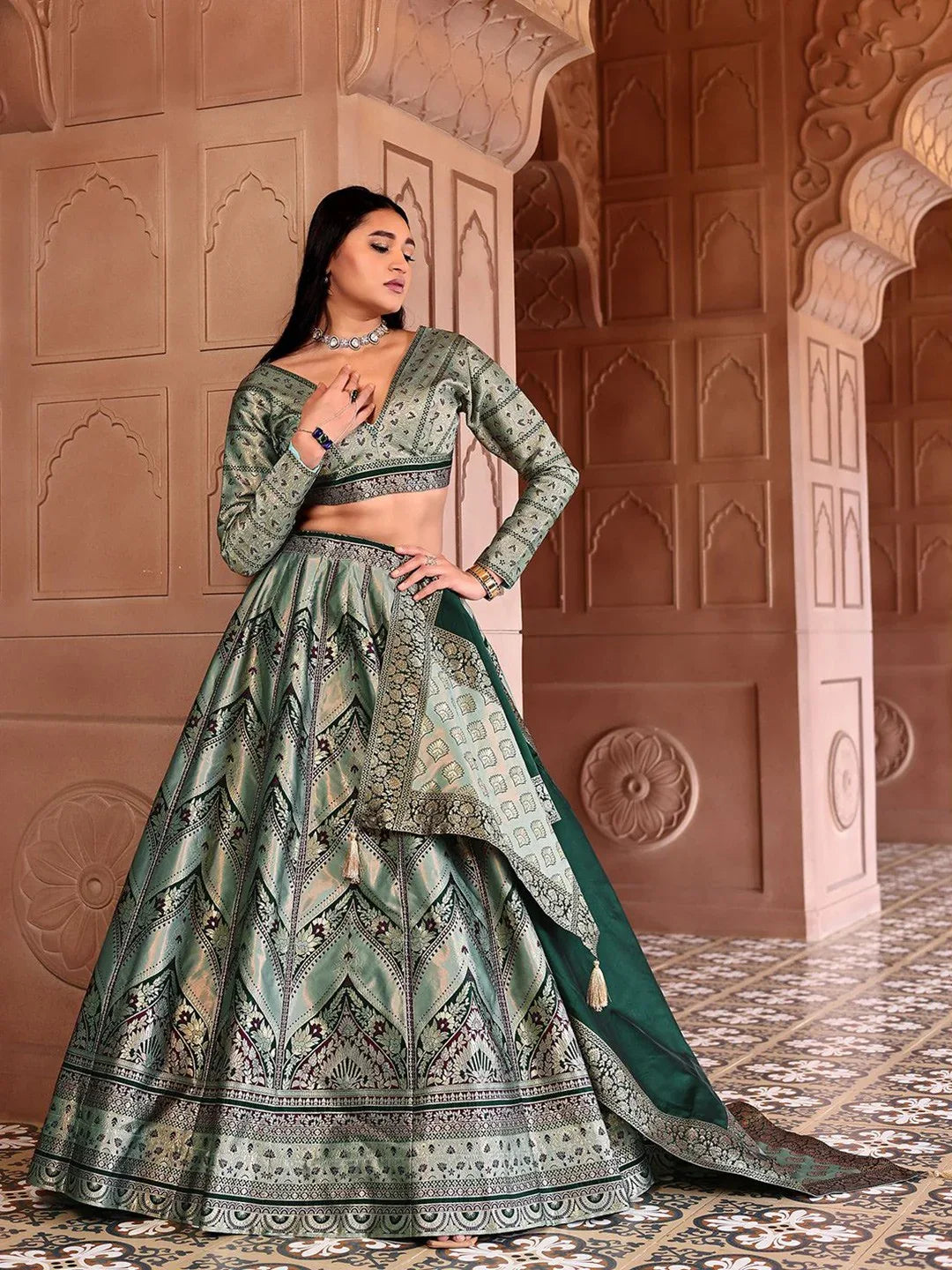 Woman in a green and gold traditional outfit standing in front of an ornate wall Glanzavi.