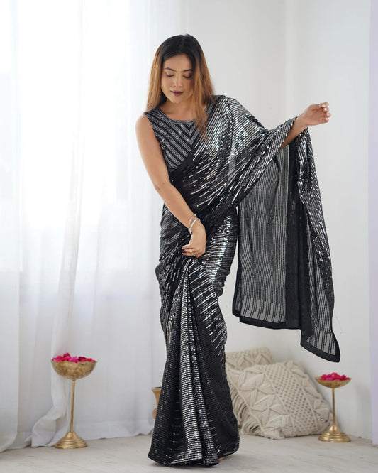 A woman modeling a silver and black sequin saree with linear embroidery and a sleeveless sequin blouse, standing in a room with a light background Glanzavi