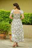 Woman in a floral dress standing outdoors with greenery in the background Glanzavi