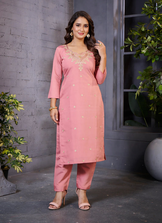 Woman wearing a pink kurta with embroidery, standing against a gray wall with plants Glanzavi