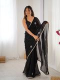 Woman wearing a black saree with white floral patterns in a minimal indoor setting Glanzavi