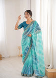 Woman wearing a blue and green saree in a room with white curtains Glanzavi.