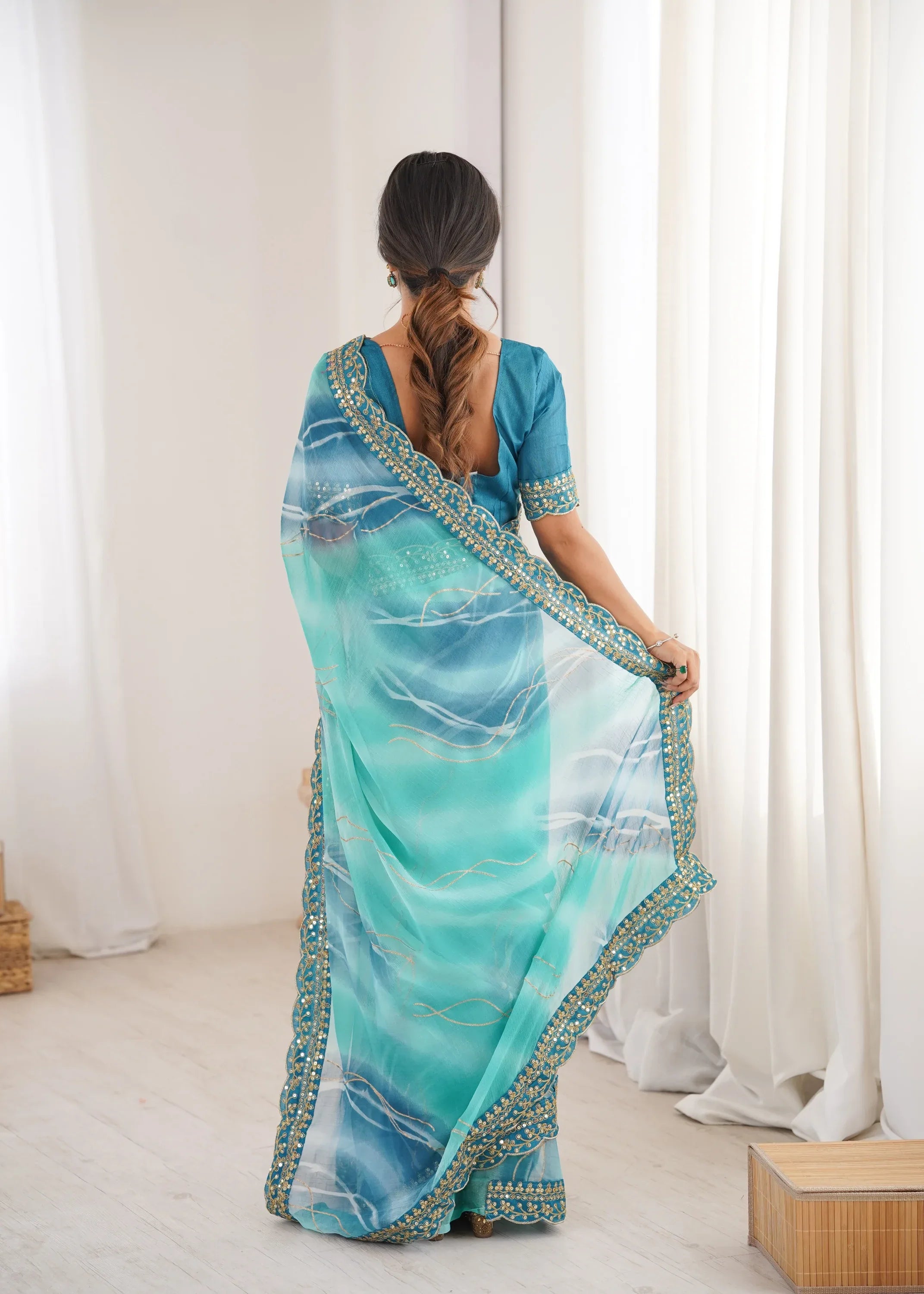 Woman wearing a blue and green saree with a white curtain background Glanzavi