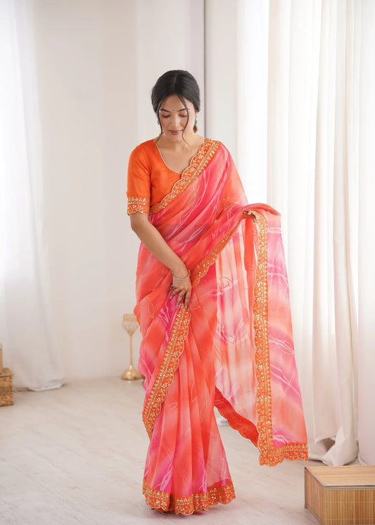 Woman wearing a vibrant orange and pink saree with gold border indoors Glanzavi.