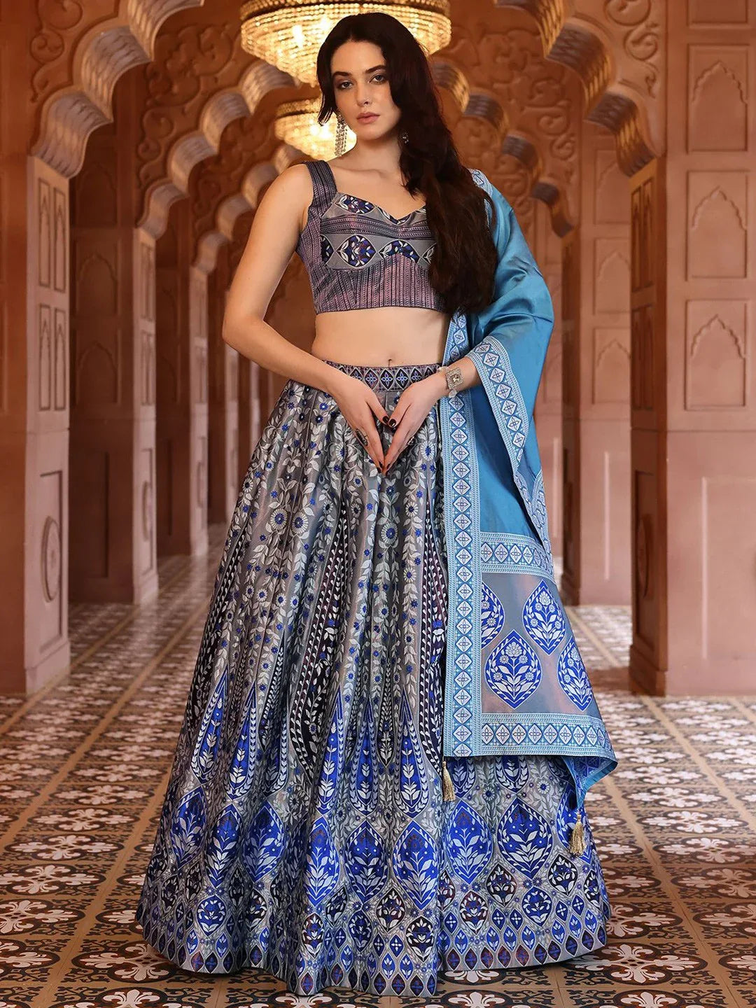 Woman in a blue and patterned traditional outfit standing in an ornate corridor Glanzavi.