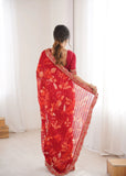 Woman wearing a red saree with floral patterns in a minimal indoor setting Glanzavi