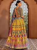 Woman wearing a traditional yellow and multicolor lehenga with intricate patterns in front of an ornate arch Glanzavi.